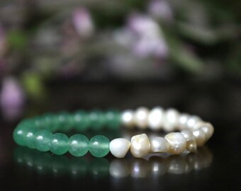 May include: A beaded bracelet featuring a combination of green aventurine and white freshwater pearls. The green beads are round and smooth, transitioning to irregular-shaped pearls. The bracelet is displayed on a dark surface.