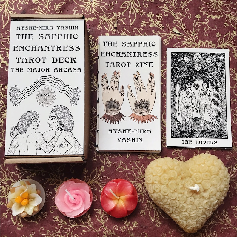 以下が含まれることがあります： 「The Sapphic Enchantress Tarot Deck」と「The Sapphic Enchantress Tarot Zine」というタイトルのタロットカードセットとジン。カードは白黒のイラストで描かれている。ジンは白い表紙に黒い文字で綴じられている。画像には、黄色、ピンク、赤の小さなろうそくも3本ある。