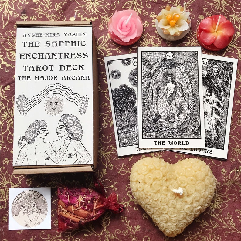 以下が含まれることがあります： 「The Sapphic Enchantress Tarot Deck」というタイトルと「The Major Arcana」というサブタイトルが書かれたタロットデッキの箱。箱が開いており、2人の人物が抱き合っている様子が描かれている。3枚のタロットカードが見え、1枚は「The World」というタイトル、もう1枚は「Lovers」というタイトルが書かれている。画像には、ハート型のろうそくなど、小さなろうそくがいくつかある。