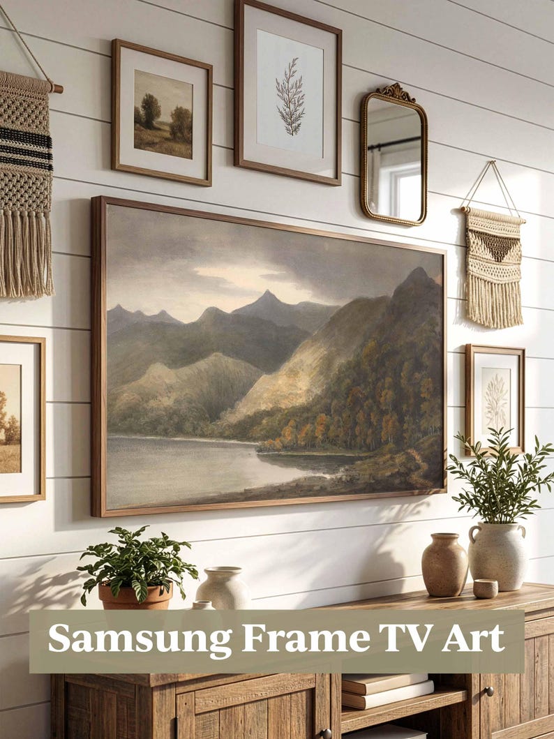 May include: A display of framed art and decorative items on a white wall, including a large landscape painting and smaller framed pictures. A wooden cabinet below holds plants and vases. The text "Samsung Frame TV Art" is visible.