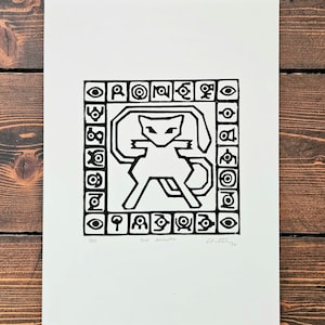Op de afbeelding: Zwart-witte print van een gestileerde kat met een geometrische patroonrand. De print is getiteld "The Ancestor" en gesigneerd "Chittagz".