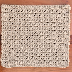 Puede incluir: Un pa&ntilde;o de cocina o toalla de cocina de crochet beige. El pa&ntilde;o est&aacute; hecho con un patr&oacute;n de punto simple y tiene una superficie ligeramente texturizada.