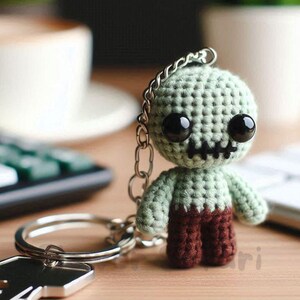 Puede incluir: Un llavero de zombi hecho a mano con ganchillo. El zombi tiene una cabeza y brazos de color verde claro, con pantalones marrones oscuros. Presenta ojos negros grandes y una boca cosida. El llavero está unido a un llavero plateado y a una llave.