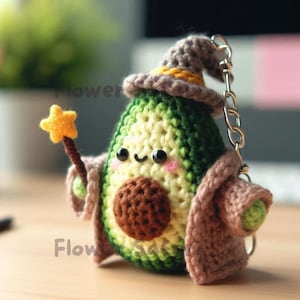 May include: A crocheted avocado keychain dressed as a wizard, complete with a pointed hat, robe, and a star-tipped wand. The avocado has a brown pit and a smiling face. The keychain is attached to a silver chain.