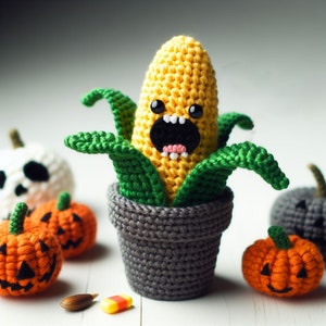 May include: A crocheted corn on the cob with a funny face, wearing a green crocheted hat and sitting in a gray crocheted pot.  Surrounding the corn are several crocheted pumpkins.