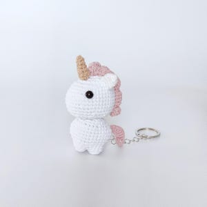 May include: White crocheted unicorn keychain with a pink mane and tail, and a gold horn. The keychain is attached to a silver metal ring.