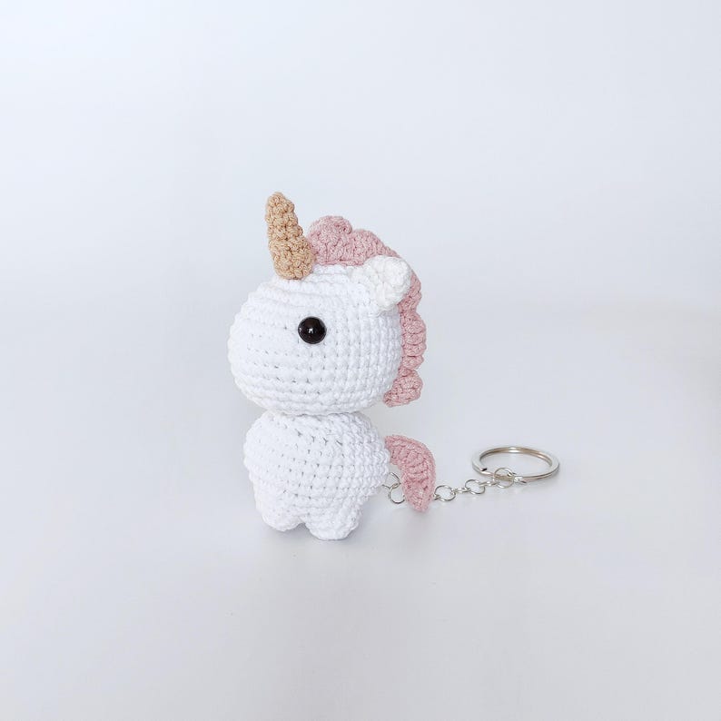 May include: White crocheted unicorn keychain with a pink mane and tail, and a gold horn. The keychain is attached to a silver metal ring.