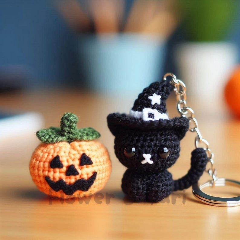 May include: Crocheted Halloween decorations: an orange pumpkin with a carved face and a black cat wearing a witch hat. The cat is attached to a keychain. The pumpkin and cat are on a wooden surface.