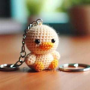Puede incluir: Un llavero de pato tejido a mano en amarillo y naranja. El pequeño pato tiene ojos negros, pico y patas naranjas. Se adjuntan una cadena y un llavero plateados.