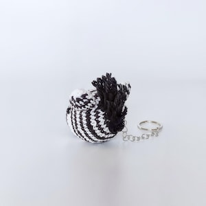 Puede incluir: Un llavero de cebra de crochet a rayas blancas y negras con una crin negra de crochet y una cadena plateada.