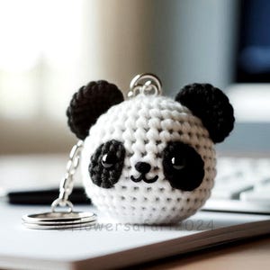 May include: A white crocheted panda bear keychain with black ears, eyes, and nose. The keychain is attached to a silver chain.