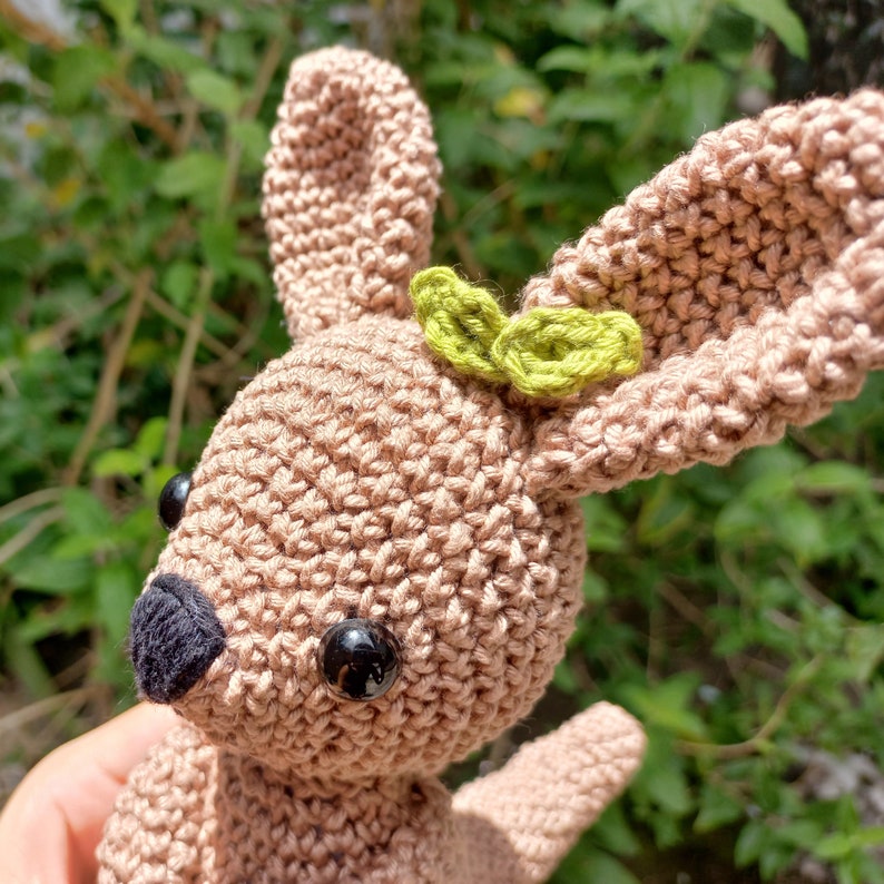 May include: A crocheted brown bunny with black eyes and a green leaf detail on its head.