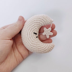 May include: A crocheted crescent moon with a small crocheted star attached. The moon is a light beige color and the star is white.