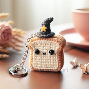 May include: A handmade crochet keychain featuring a slice of toast with a smiling face and a small witch hat with a yellow star. The keychain has a silver chain and ring.