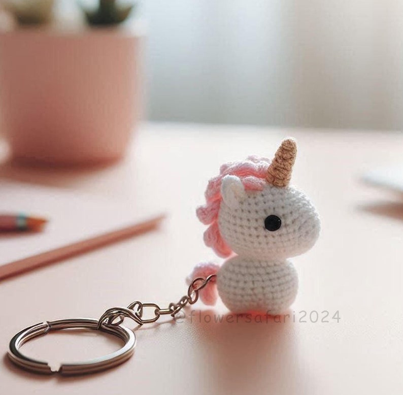 May include: White crocheted unicorn keychain with pink mane and a gold horn. The keychain has a silver metal ring.