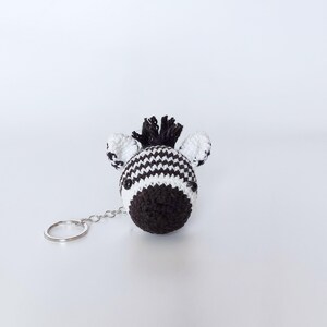 Puede incluir: Un llavero de cebra de crochet blanco y negro con un anillo de llave plateado.