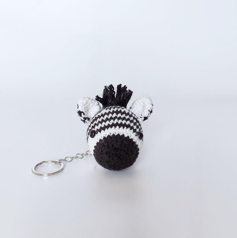 Puede incluir: Un llavero de cebra de crochet blanco y negro con un anillo de llave plateado.
