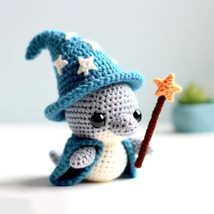 Puede incluir: Un pingüino de crochet gris y blanco con un sombrero de mago azul con estrellas blancas y sosteniendo una varita marrón y naranja.