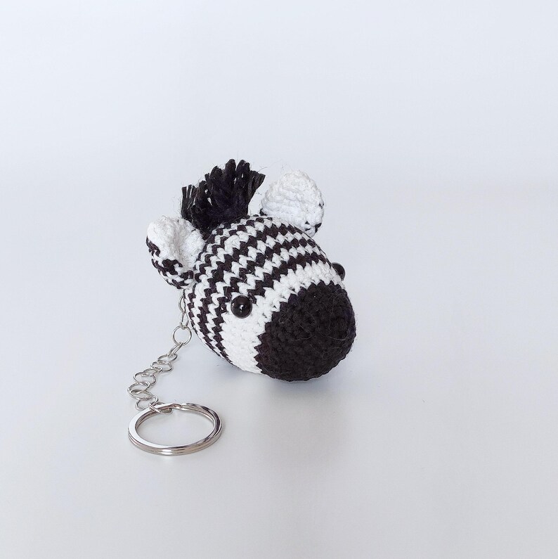 Puede incluir: Un llavero de cebra de crochet blanco y negro con un anillo de llave plateado.