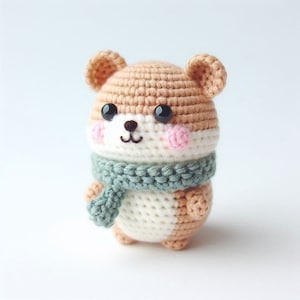 May include: A handmade crochet hamster doll with a light brown and white body, black eyes, pink cheeks, and a green scarf. The amigurumi animal has small ears and a smiling face. The doll is a cute, soft toy.