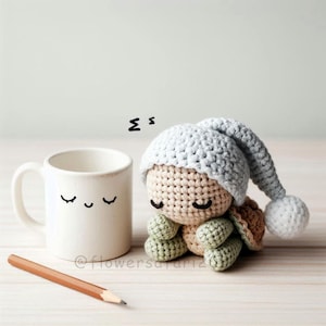 Puede incluir: Una tortuga de crochet con un gorro de dormir de crochet gris con un pompón blanco. La tortuga tiene los ojos cerrados y está sentada sobre una superficie de madera. El texto "z z" está escrito sobre la tortuga.