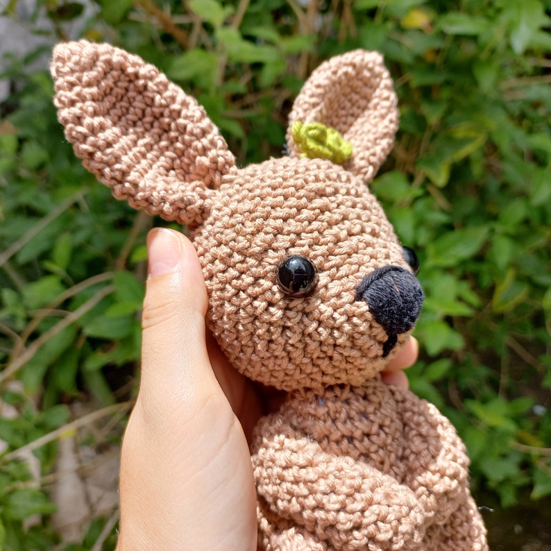 May include: A crocheted brown bunny with black eyes and a green flower on its head.