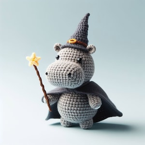 Op de afbeelding: Een grijze gehaakte nijlpaard met een paarse tovenaarshoed met een gele ster erop en een paarse cape. Het nijlpaard houdt een bruine stok vast met een gele ster erop.