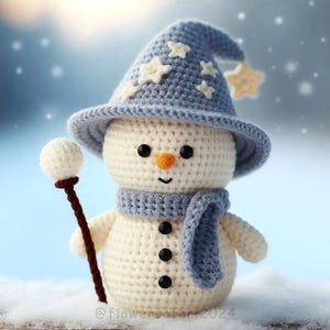 May include: A crocheted snowman wearing a blue and white star patterned hat and a blue scarf, holding a white ball on a stick.