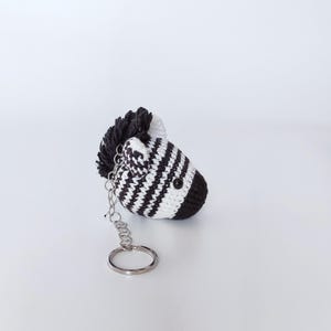 Puede incluir: Un llavero de cebra de crochet blanco y negro con un anillo de llave plateado.