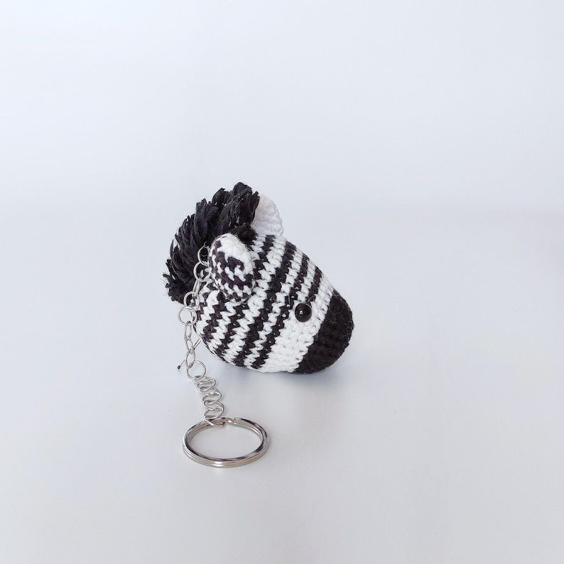 Puede incluir: Un llavero de cebra de crochet blanco y negro con un anillo de llave plateado.