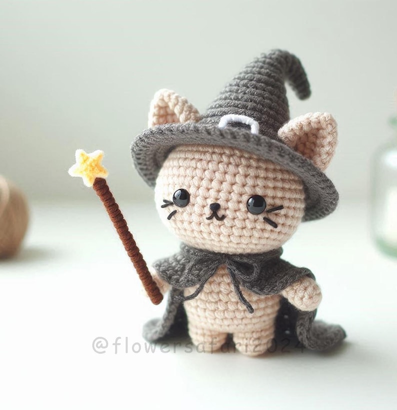 May include: A crocheted cat figurine wearing a gray witch hat and cape, holding a brown wand with a yellow star. The cat has black eyes and whiskers. The figurine is beige and gray.