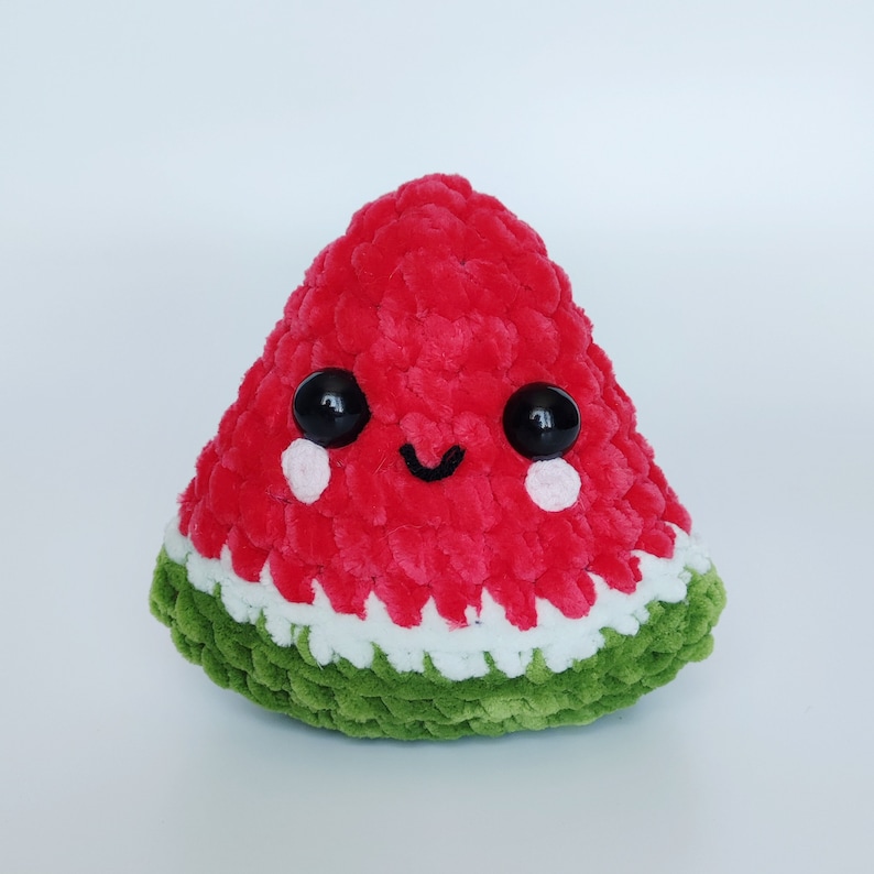 May include: A red and green crocheted watermelon plush toy with a smiling face and black eyes.