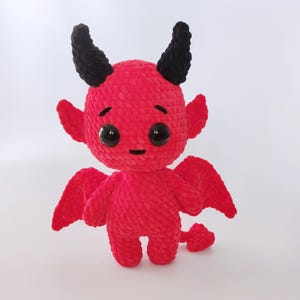 Pode incluir: Uma boneca de diabo vermelha de crochê feita à mão com chifres, asas e cauda pretas. A boneca tem olhos grandes e pretos e um pequeno sorriso. O brinquedo de pelúcia é uma criação caprichosa e única.