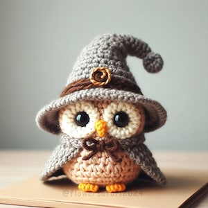 Puede incluir: Un búho de crochet que lleva un sombrero de bruja gris con una banda marrón y un acento de espiral dorado. El búho tiene grandes ojos negros, un pico marrón y una pajarita marrón. El búho está de pie sobre una superficie marrón.