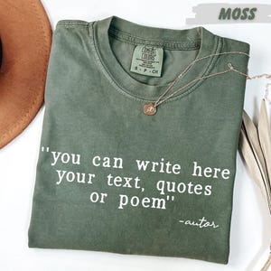 a green t-shirt with a quote printed on it, along with a brown hat and some dried leaves, all placed on a white surface.
