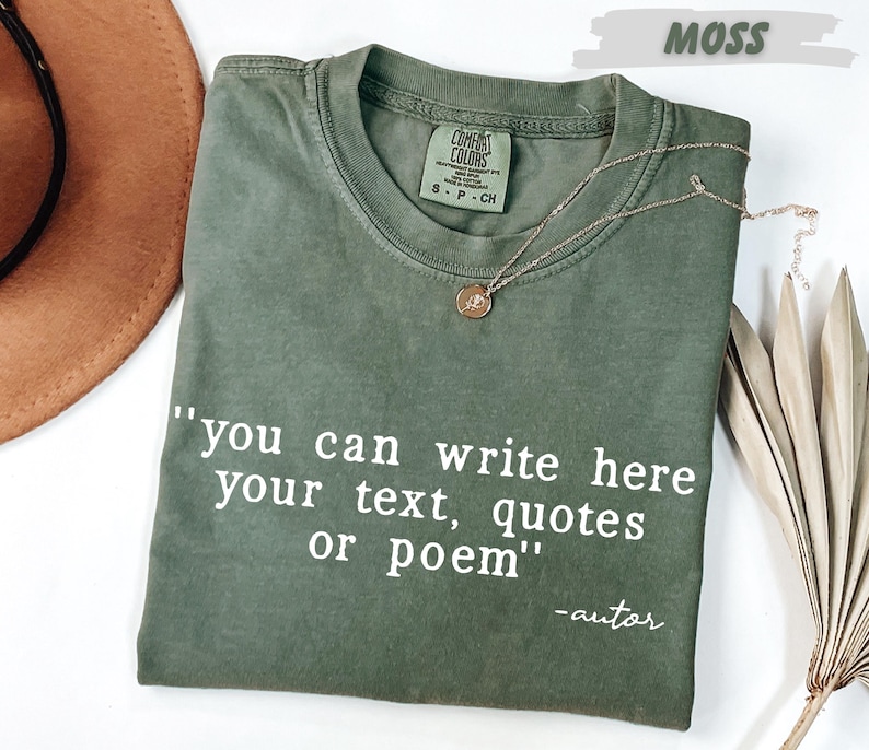 a green t-shirt with a quote printed on it, along with a brown hat and some dried leaves, all placed on a white surface.