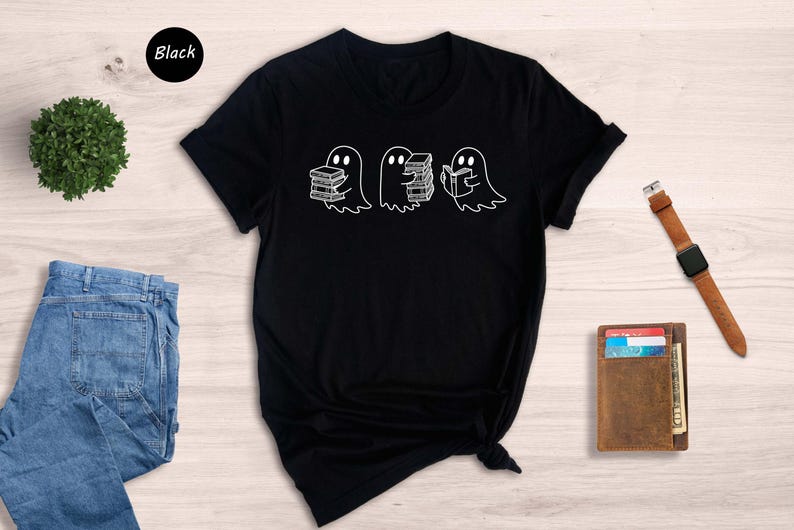 May include: Black t-shirt featuring a graphic of three ghosts interacting with books. One ghost carries a stack of books, another holds a single book, and the third ghost appears to be reading a book. The design is simple and minimalist, with white outlines on a black background. The word 'Black' is visible in the upper left corner, indicating the shirt's color.