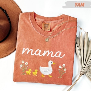 a pink t-shirt with a white duck and two yellow ducklings, along with a brown hat and a fan, all arranged on a white background.