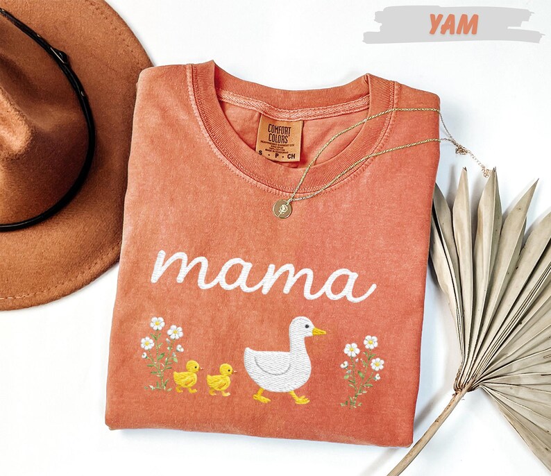 a pink t-shirt with a white duck and two yellow ducklings, along with a brown hat and a fan, all arranged on a white background.