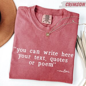 a red t-shirt with a quote printed on it, along with a necklace and a hat, all placed on a white surface.