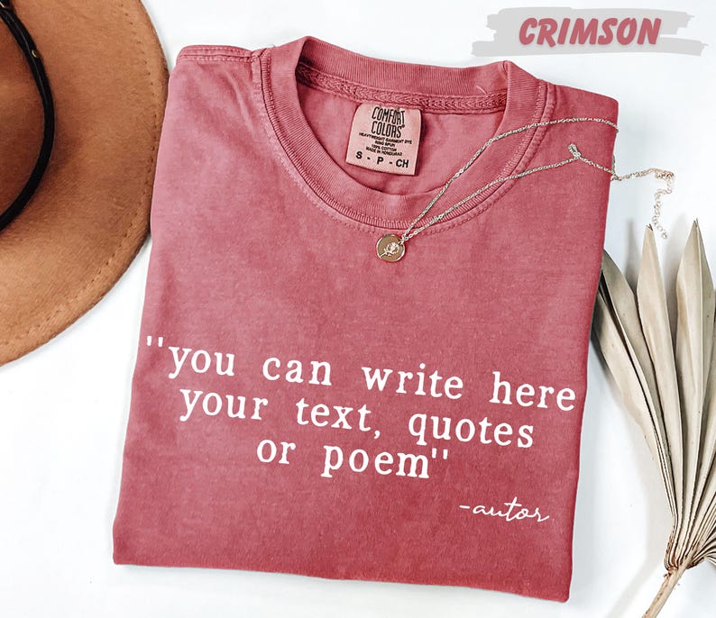 a red t-shirt with a quote printed on it, along with a necklace and a hat, all placed on a white surface.