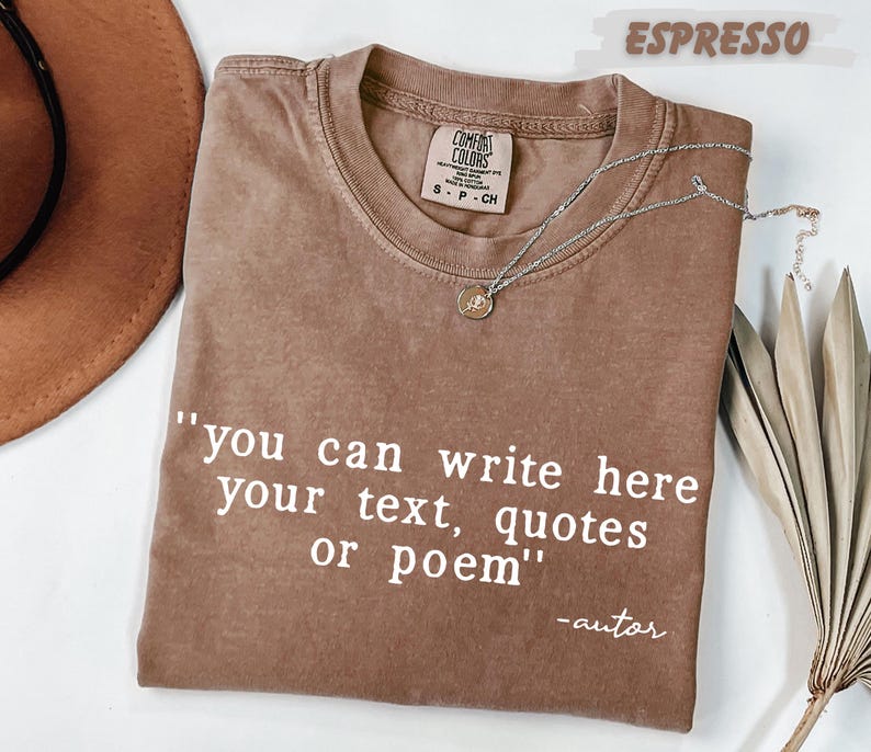 a brown t-shirt with a quote printed on it, along with a hat and some dried leaves, all placed on a white surface.