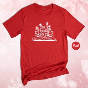 May include: A red t-shirt with a white graphic of a book with flowers growing out of it. The text 'Red' is visible in the lower right corner of the image.