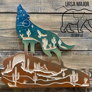 Op de afbeelding: Houten wandkunst met een silhouet van een huilende wolf met een woestijnlandschap erin. De wolf is omlijnd in blauw en groen met sterren en een halve maan. Het woestijnlandschap is in tinten bruin en beige met cactussen en een kleine vogel.