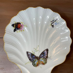 May include: A white porcelain shell-shaped dish with a gold rim, featuring three butterflies with colorful wings. The butterflies are painted in a realistic style with intricate details.