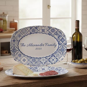May include: Oval serving platter and matching plate with a blue and white floral design. The platter has the text "The Alexander Family 2025". The plate holds cheese and salami. A bottle of wine and glasses are in the background.