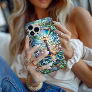 May include: A colorful phone case featuring a lighthouse design. The case has a stained-glass style with a lighthouse, ocean waves, and a sunset. The case is primarily blue, green, and yellow.