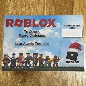 May include: A Christmas card with a Roblox theme. The card features a group of Roblox avatars, including a robot, a knight, and a pirate. The card also includes the text "To Carson, Merry Christmas Love Auntie Jem xxx" and a space for a voucher code.