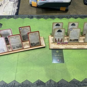 May include: A wooden game organizer with slots for cards. The organizer has a brown stain and is labeled with numbers. The cards are for a board game and have titles like "Infantry Major Leader" and "Bombard."