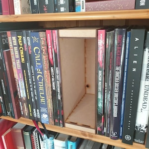 May include: A bookshelf with a variety of books, including several with titles related to role-playing games, such as "Call of Cthulhu" and "Dungeons & Dragons".